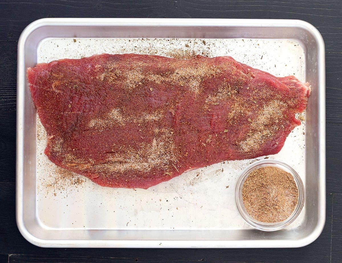 flank steak coated in steak run on a silver baking sheet.