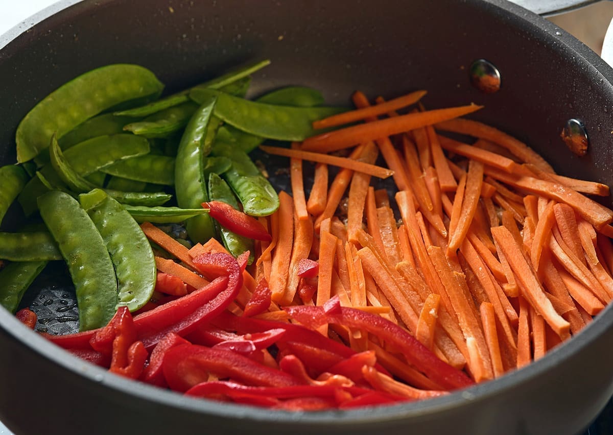 Sliced snow peas, carrots and red bell pepper in a pan.