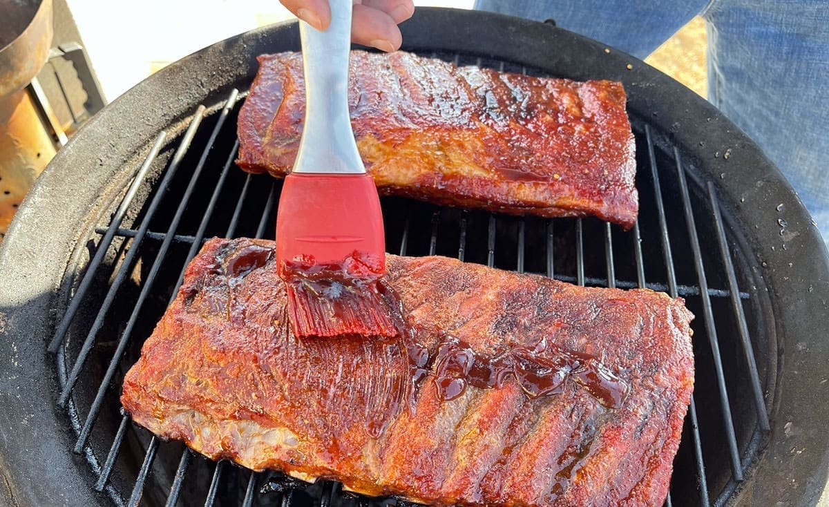 3-2-1 ribs being coated in BBQ sauce on the grill.