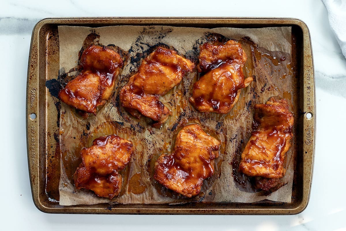 Poultry coated in barbecue sauce on a baking sheet.