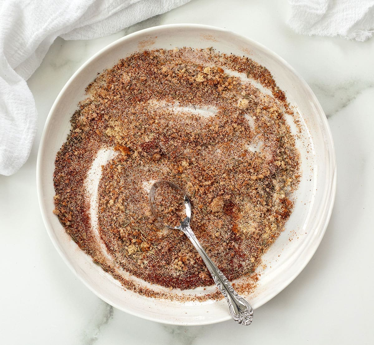 Smoke rub for chicken spices on a white plate with a silver spoon.