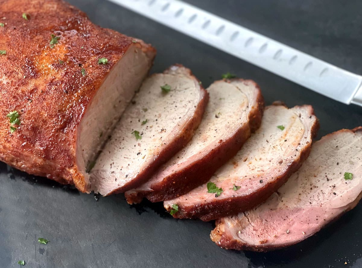 Sliced pork on a black cutting board.