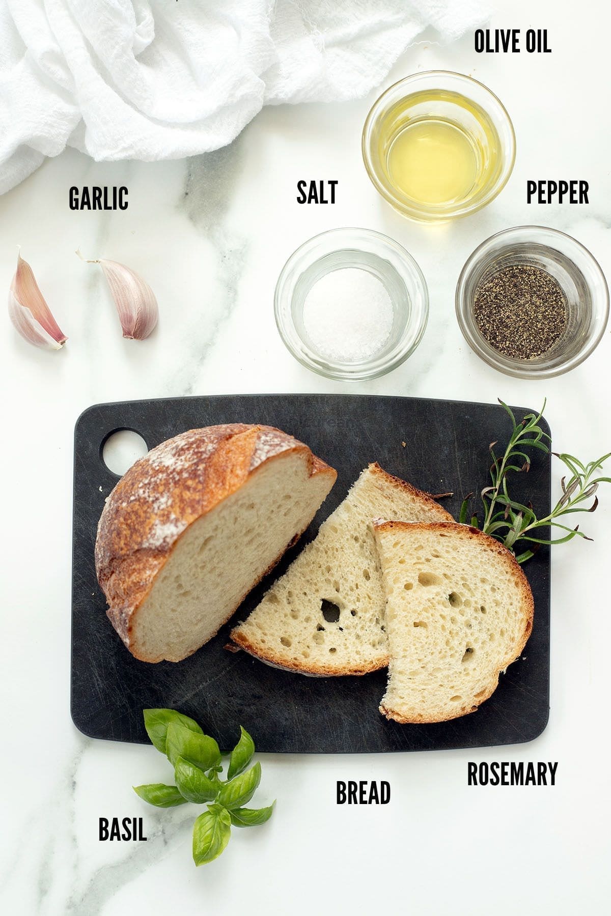 Bread, herbs and seasoning next to a black cutting board.