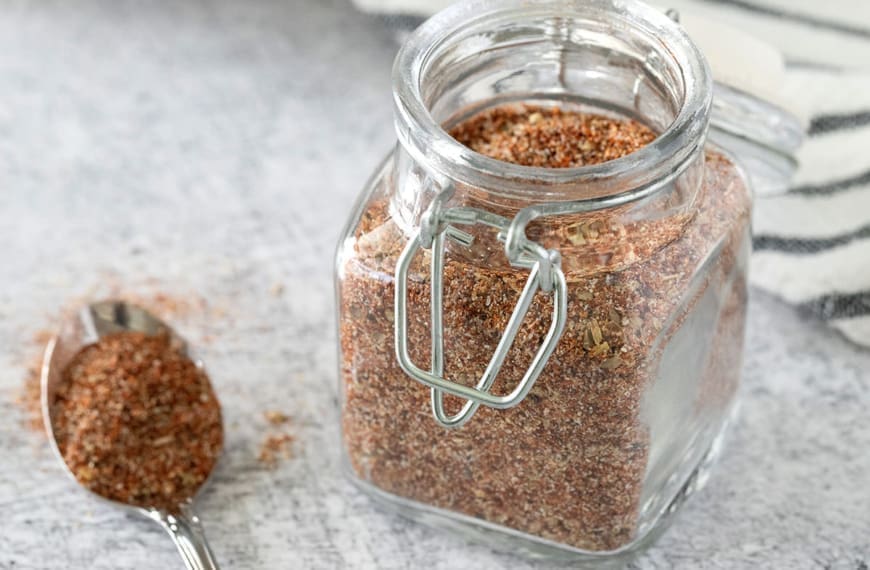 Steak rub in a small glass jar and on a small spoon.