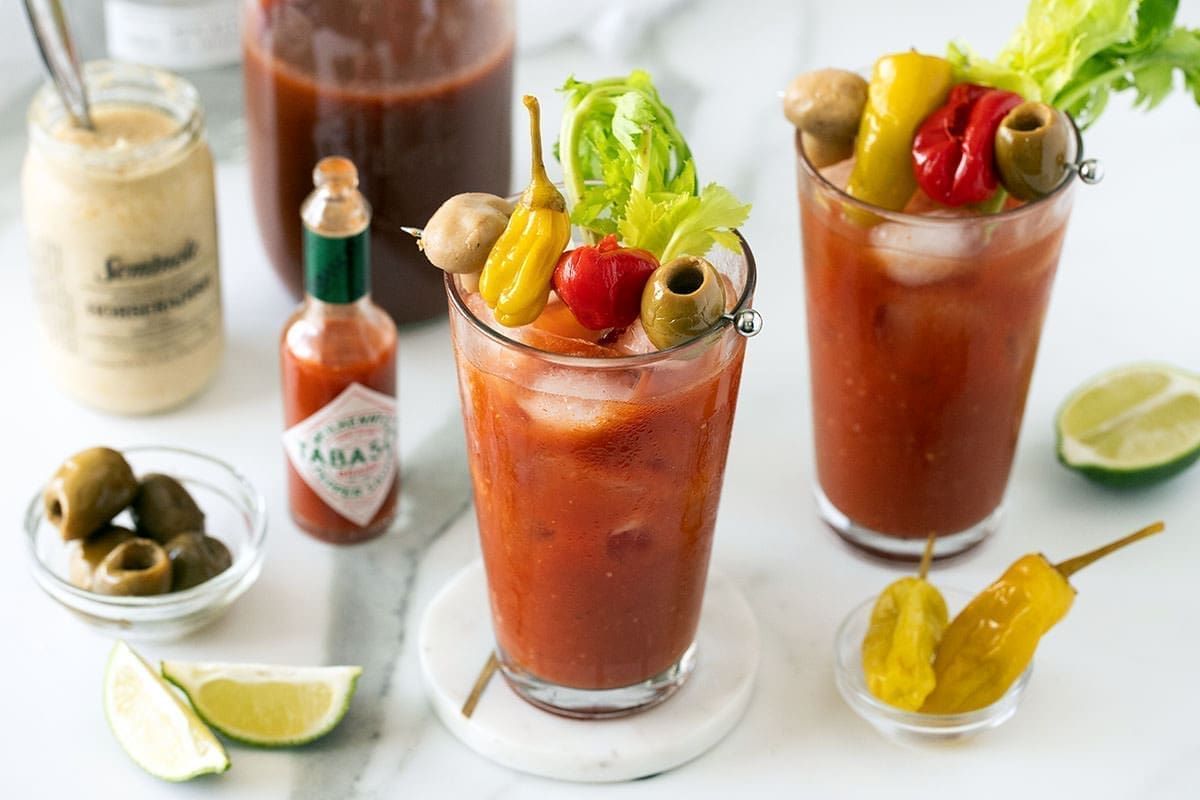 Two Bloody Caesar Drinks with bowls of garnish.