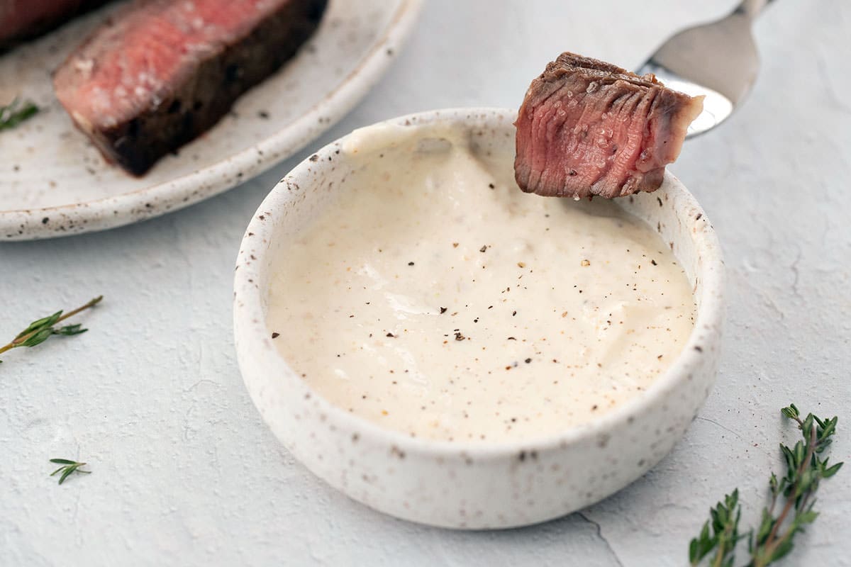 Bite of steak being dipped into a bowl of horseradish sauce for beef tenderloin.