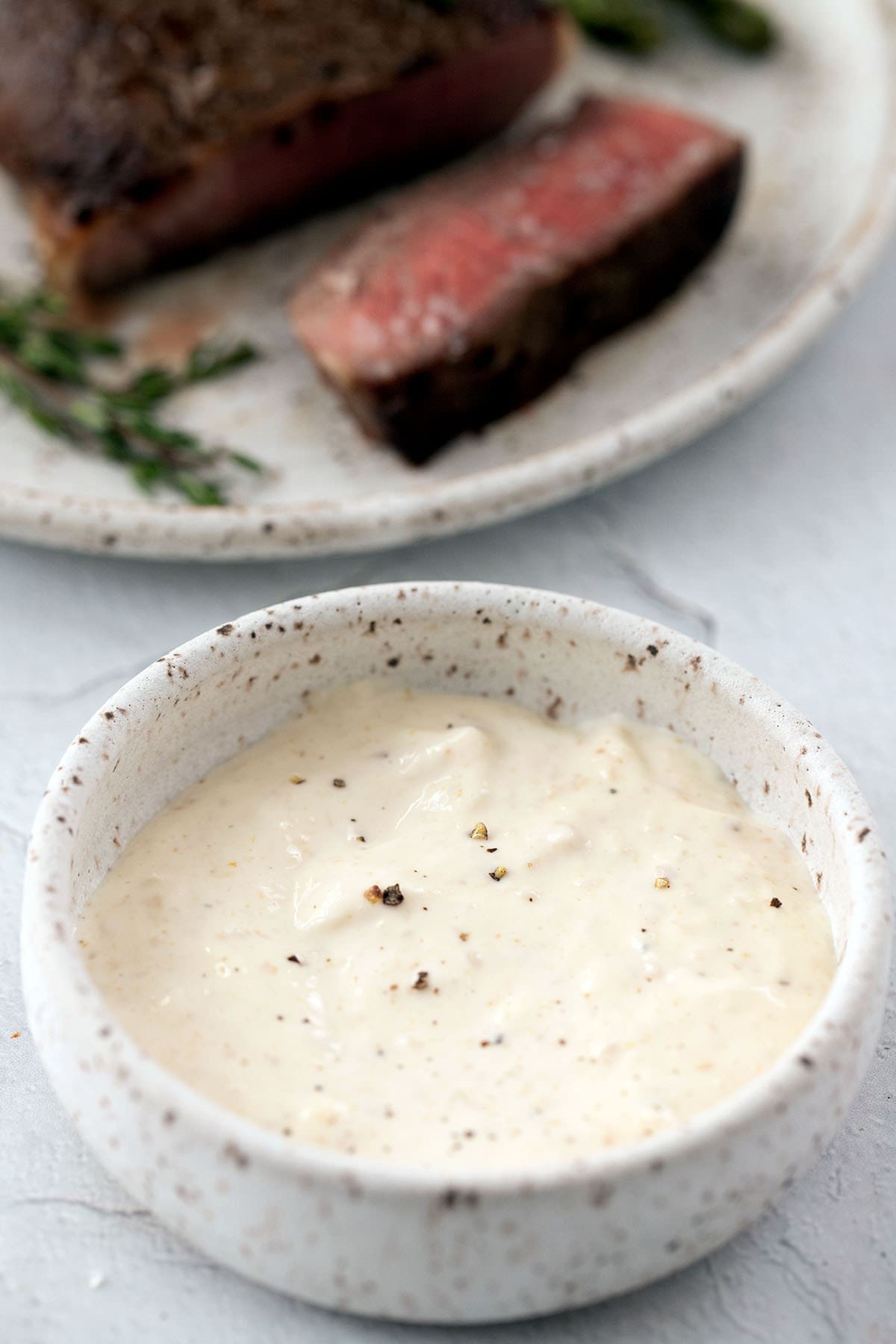 Bowl of horseradish sauce with sliced beef tenderloin in the background.