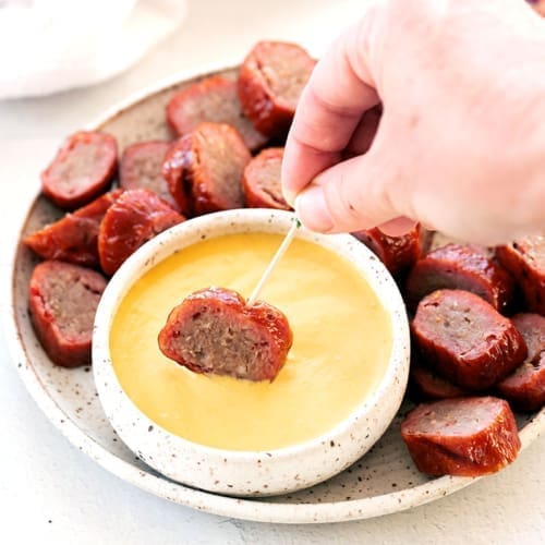 Smoked sausage on a toothpick being dipped in a mustard sauce.