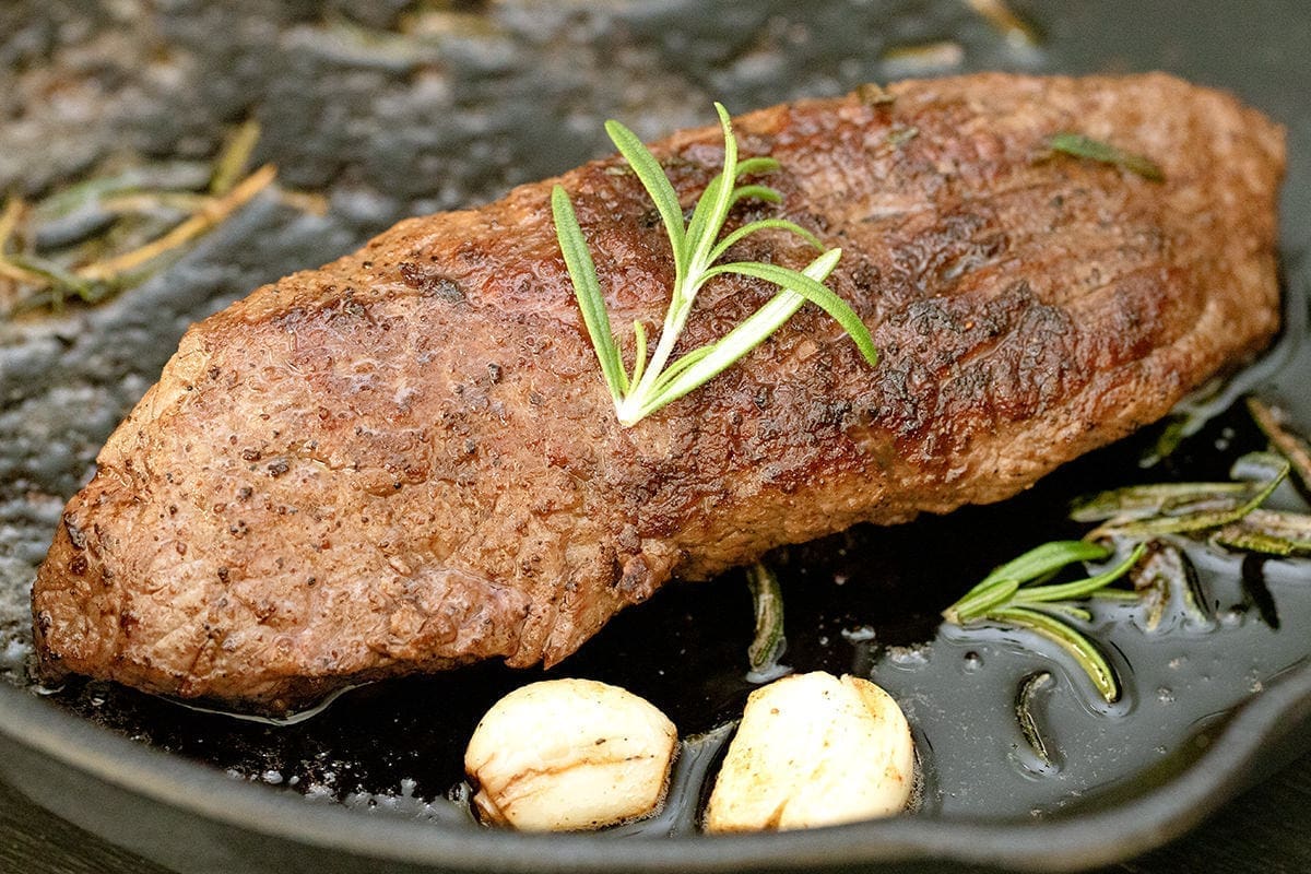 Teres Major Steak on a cast iron skillet with garlic and rosemary.