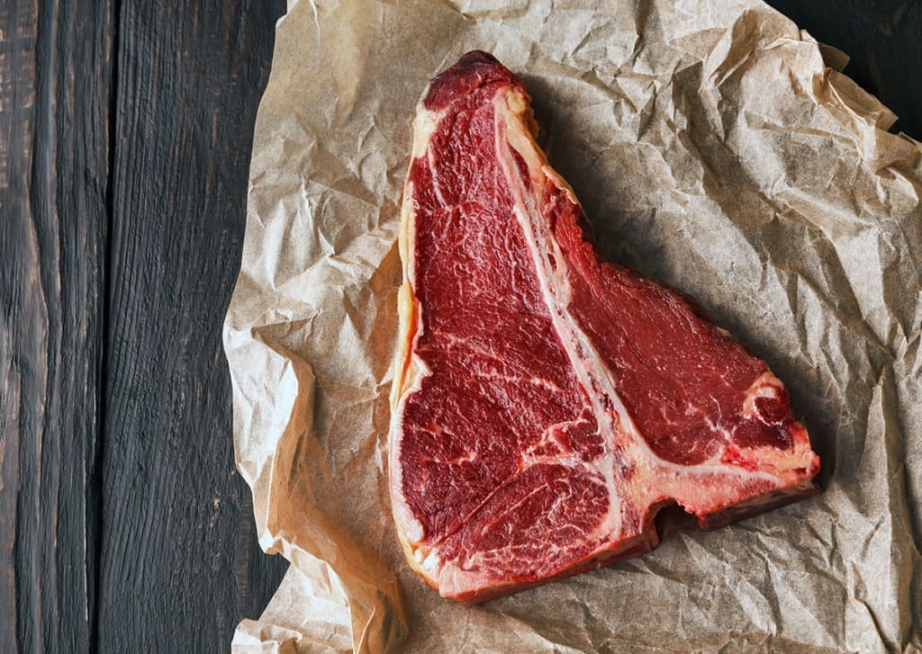 Raw t-bone steak on crumpled parchment paper for best steak for grilling article.