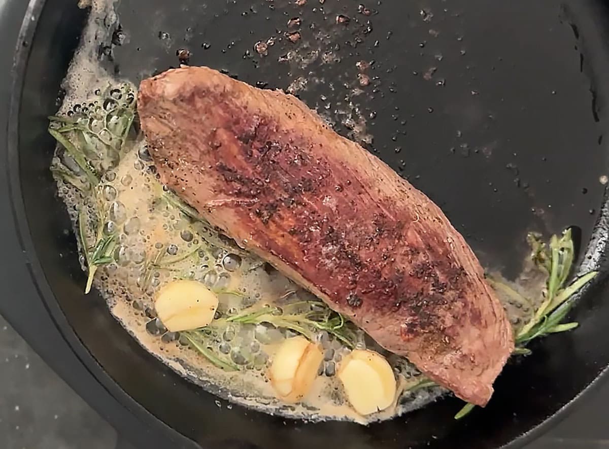 cooked steak with melted butter and garlic cloves in a hot skillet.