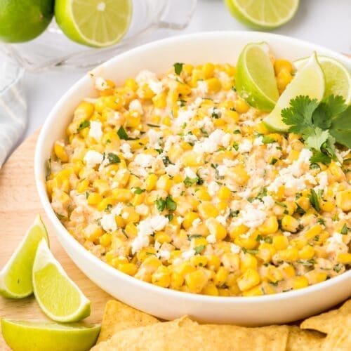 Elote dip in a white bowl with chips and limes.
