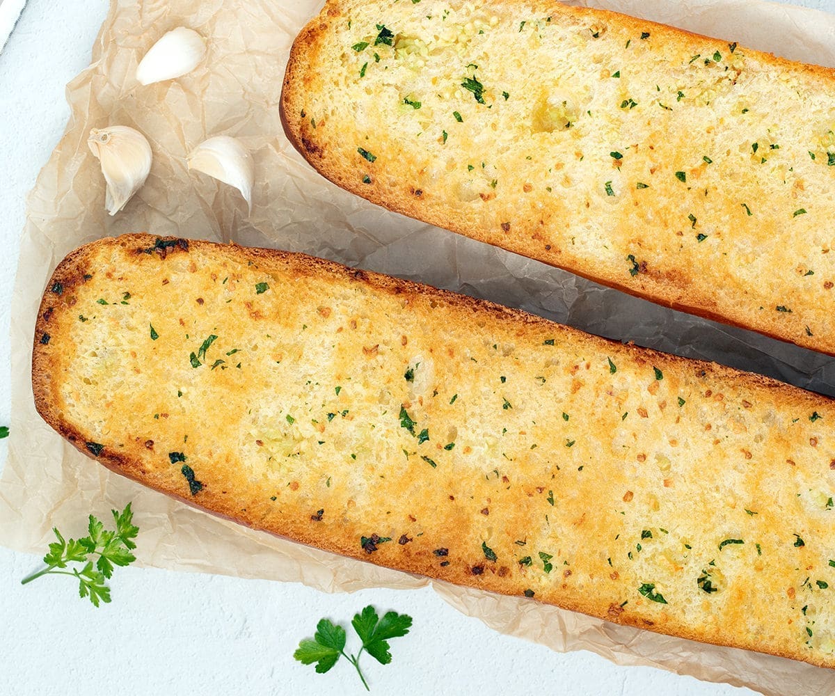 Homemade Garlic Bread recipe next to garlic cloves and parsley.