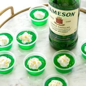 8 green jello shots next to a bottle of Jameson Whiskey.