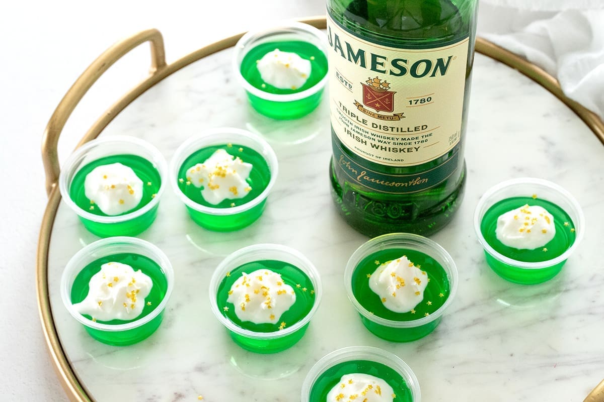 8 green jello shots next to a bottle of Jameson Whiskey.