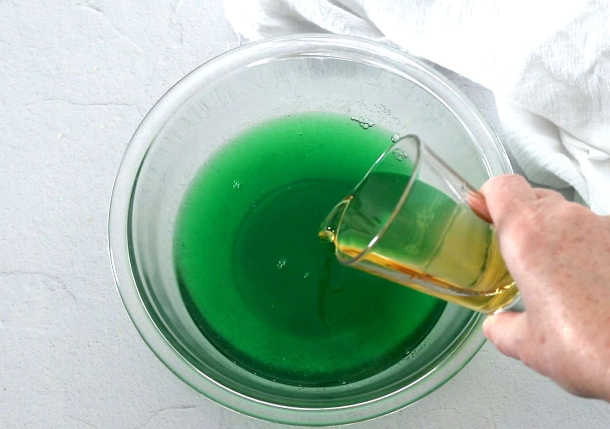 Hand pouring alcohol into a bowl of green liquid.