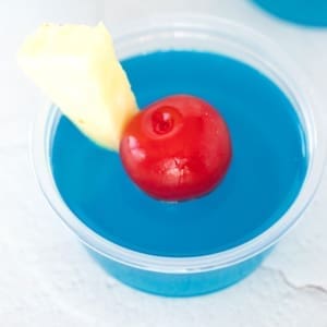 Blue Hawaiian Jello Shots garnished with a cherry and pineapple slice.