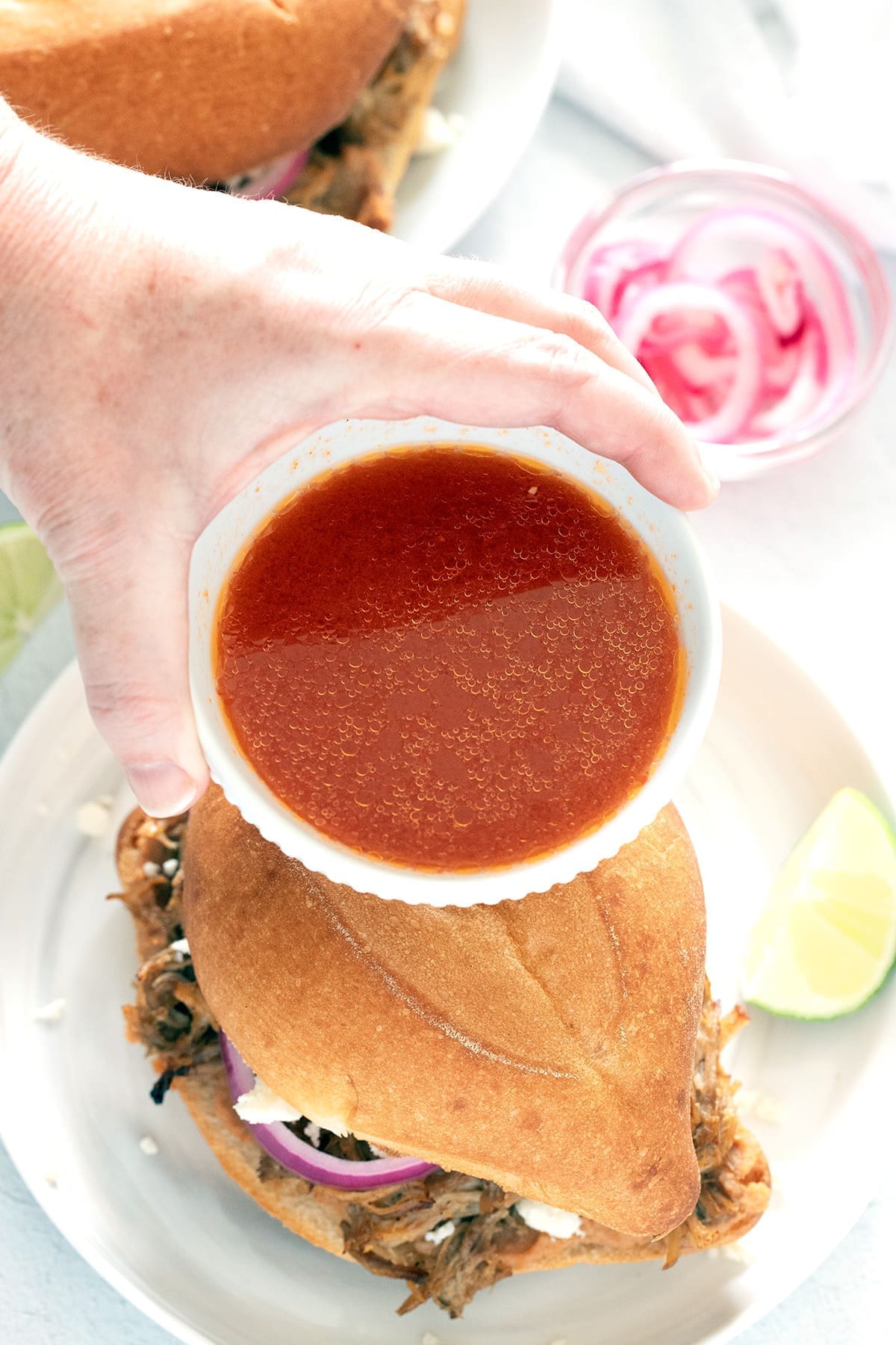 hand holding red chili sauce over a Mexican sandwich.