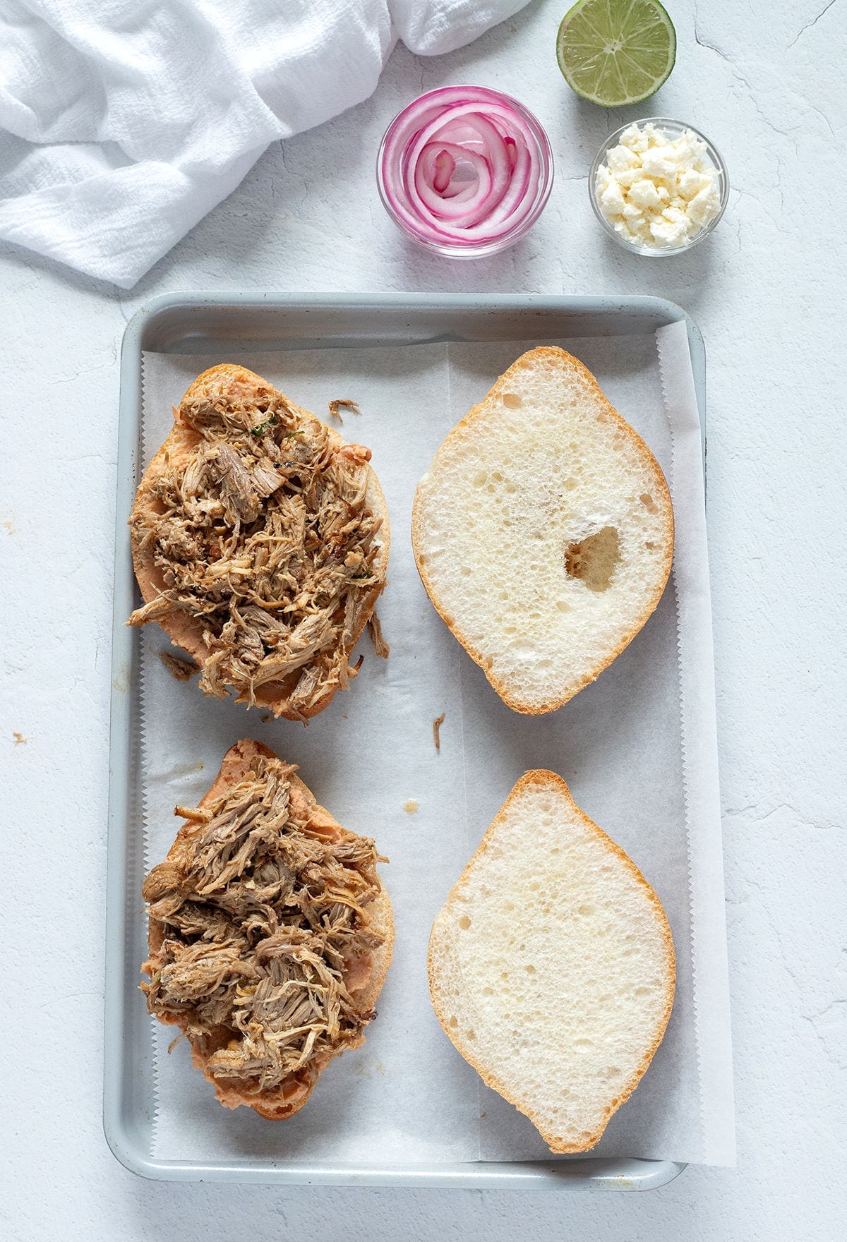 Mexican bread topped with carnitas on a baking sheet.
