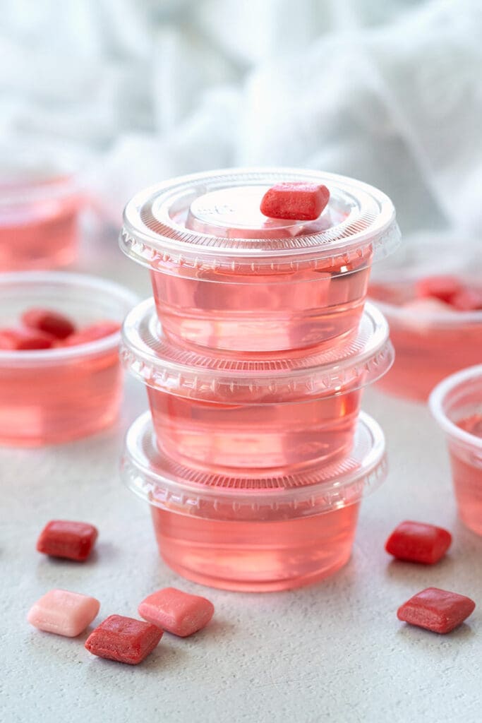 stacked jello shots with small pieces of pink and red candy.