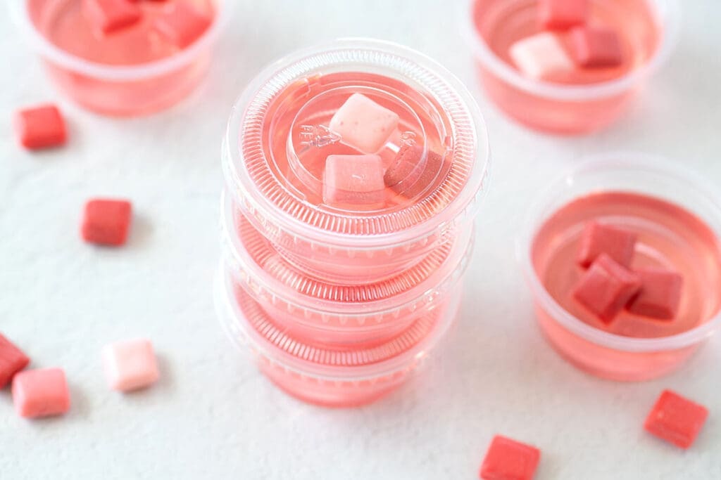 Pink Jello Shots stacked on top of each other next to mini Starburst candies.