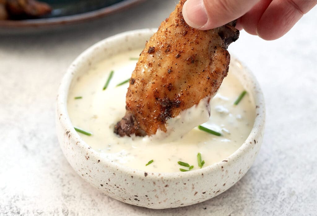 Hand dipping a wing into ranch dipping sauce.