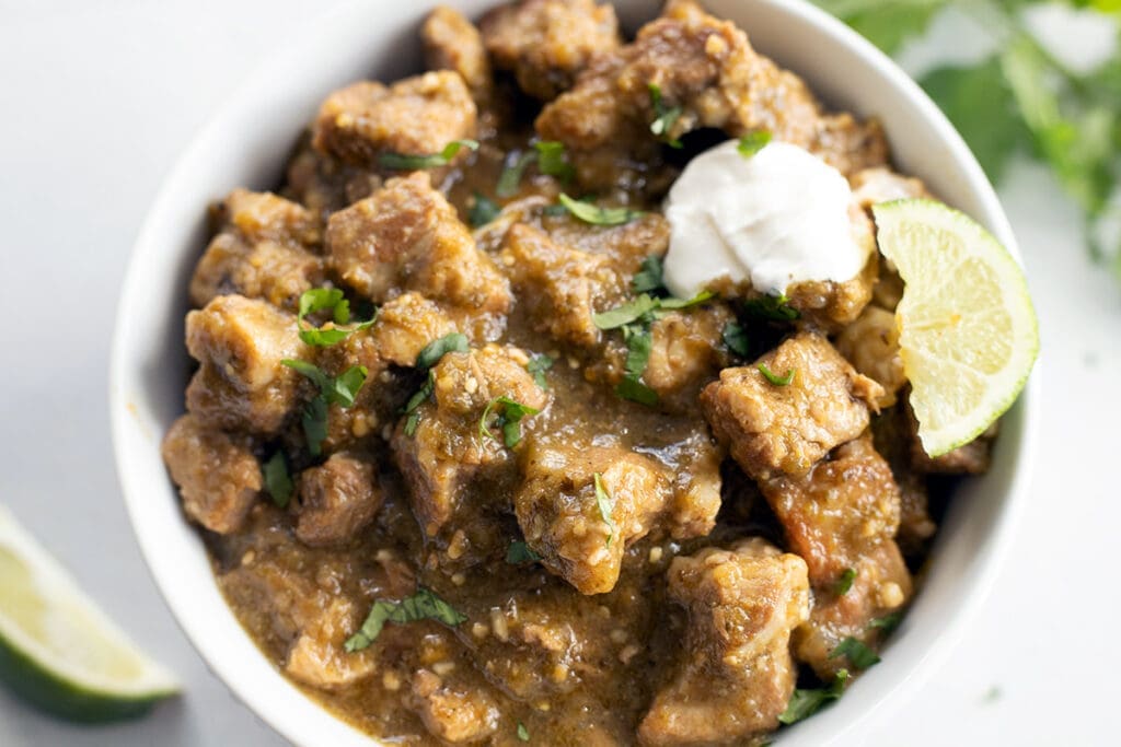 Bowl of green chile verde topped with lime and sour cream.