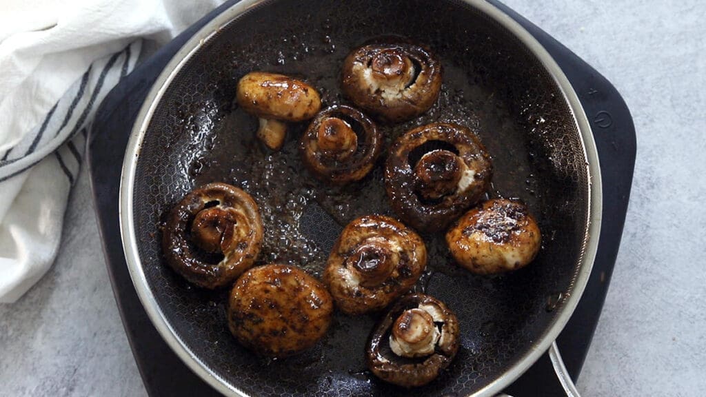 Mushrooms simmering in a sauce in a skillet.