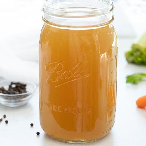 Mason Jar full of golden vegetable broth surrounded by raw veggies.