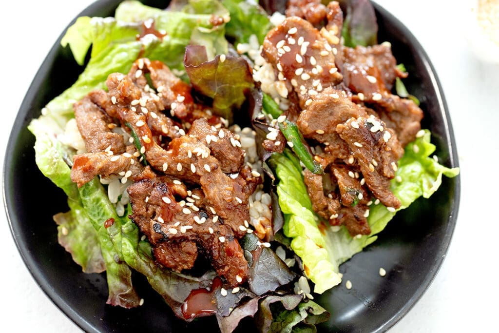 Two bulgogi lettuce wraps on a black plate.