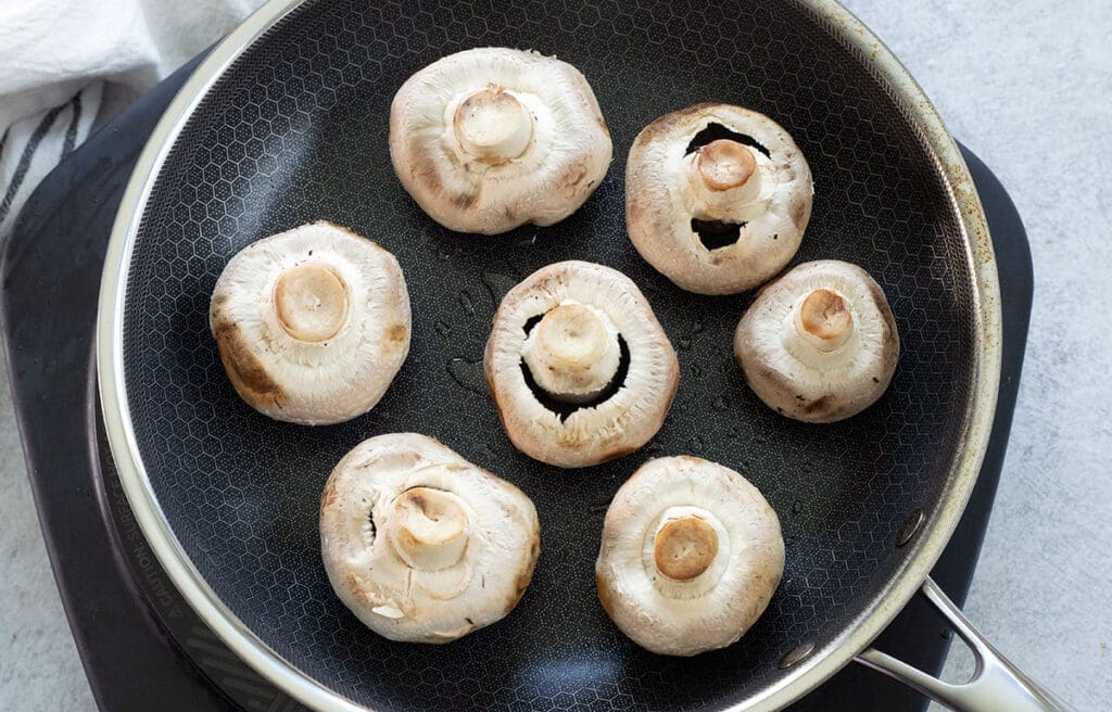 Upside down mushrooms in a black skillet.