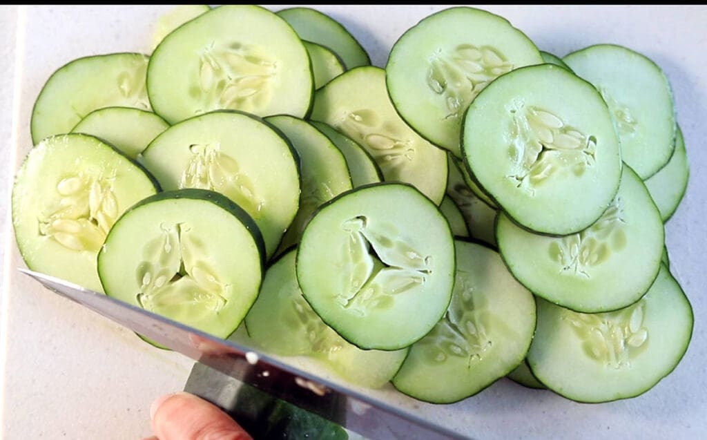 Sliced cucumbers on a white cutting board.