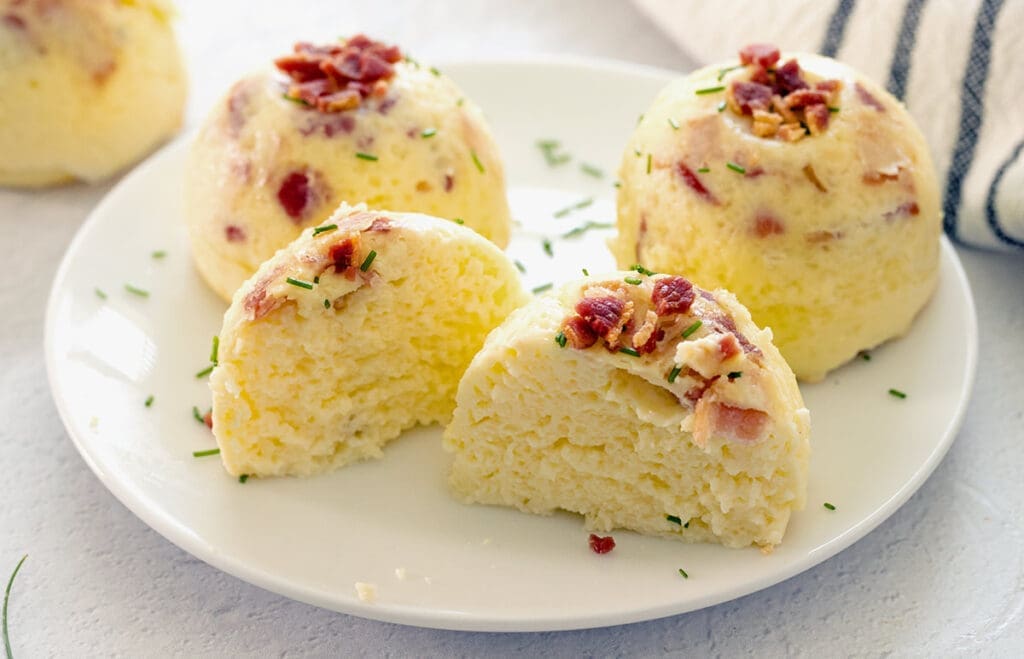 Three bacon egg bites on a white plate with one cut in half.