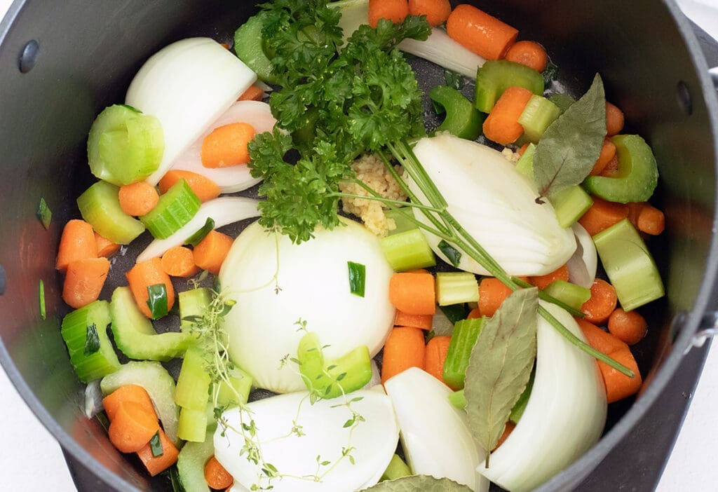Variety of vegetables to make vegetable stock in a black stock pot.