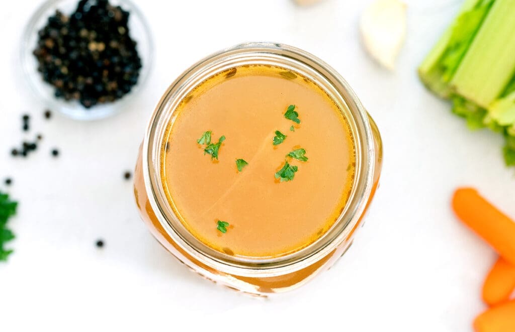 Jar of stock next to black pepper, carrots and celery.