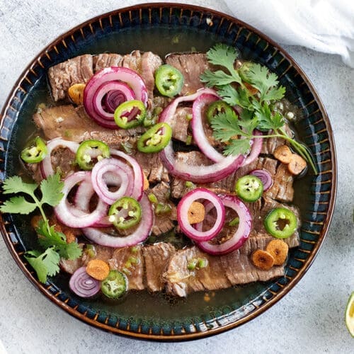 Steak Aguachile Verde on a blue plate surrounded by sliced citrus fruit.