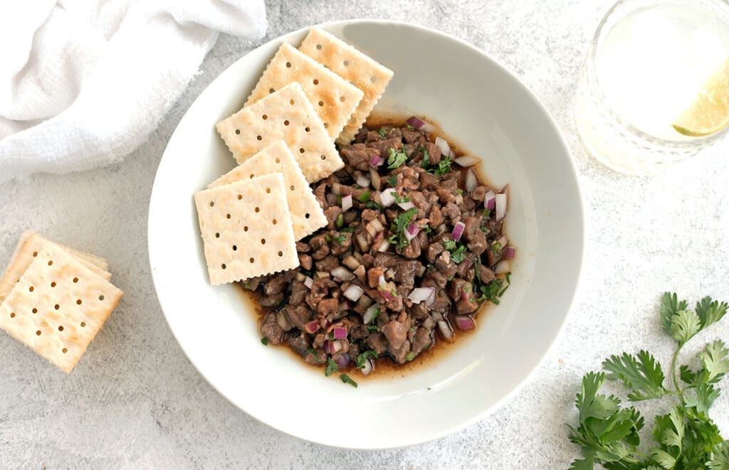 Steak tartare in a white bowl next to crackers.