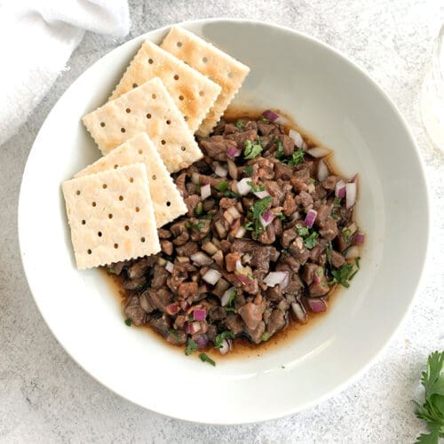 Steak tartare in a white bowl next to crackers.