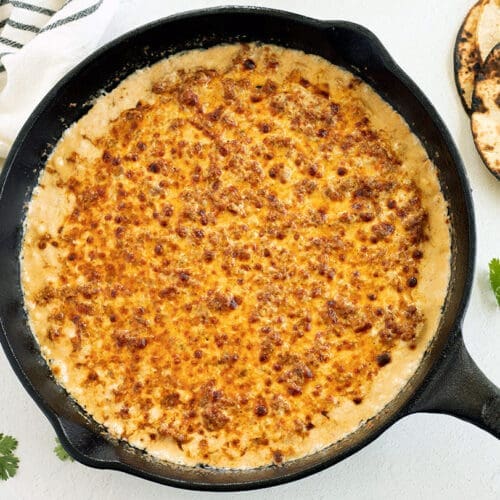 Choriqueso in a cast iron skillet next to cilantro and tortillas.