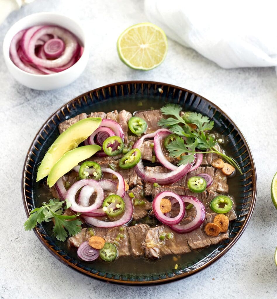 Steak aguachile verde on a dark blue plate.