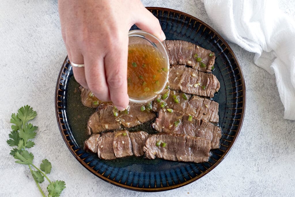 Plate of sliced filet mignon with a hand pouring marinade over it.