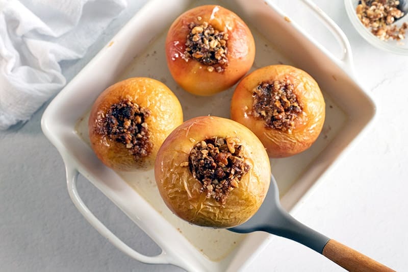 4 baked apples in a white baking dish. 