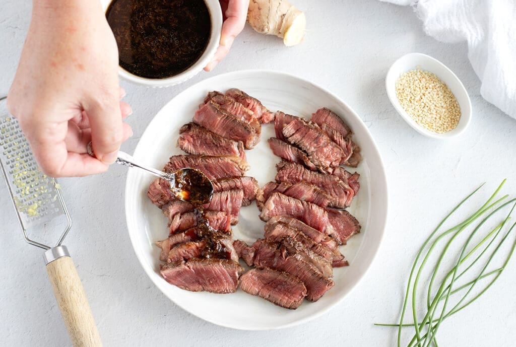 A hand drizzling ponzu sauce over sliced beef.