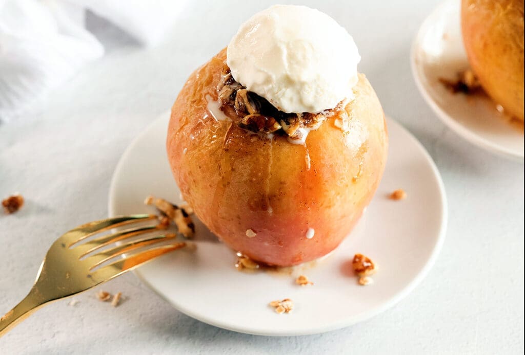 baked apple on a white plate topped with vanilla ice cream.