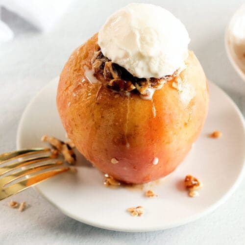 baked apple on a white plate topped with vanilla ice cream.