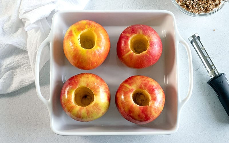 Four cored apples in a white baking dish.