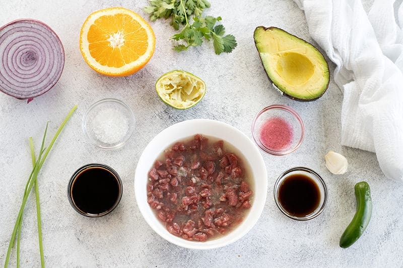 Minced beef in a white bowl surrounded by citrus fruit and sauces.