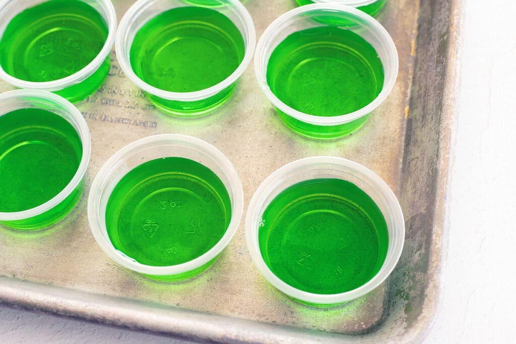 green gelatin in plastic cups on a baking pan.