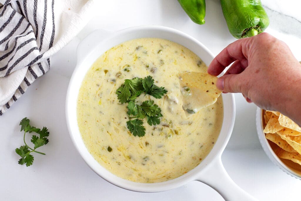 Hand holding a chip dipping into hatch green chile queso.