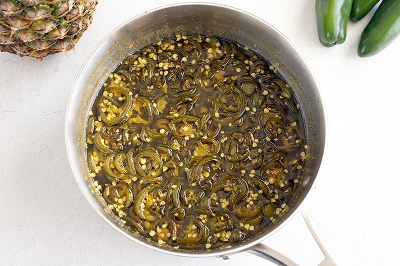 Cooked green peppers in a silver sauce pan.